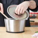 A person stirring food in a Vollrath stainless steel sauce pan.