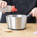 A person pouring seasoning into a Vollrath stainless steel sauce pan.