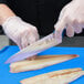 A person in gloves using a Mercer Culinary Millennia Colors chef knife to cut fish.