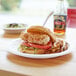 A chicken sandwich with tomato and lettuce on a white Eco-Products compostable plate with fries and a drink on a table.