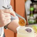 A person using Mercer Culinary curved plating tongs to add a lime wedge to a drink.