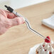 A person using Mercer Culinary offset plating tongs to place a raspberry on top of a dessert.