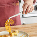 A person using Mercer Culinary curved plating tongs to place a slice of lemon pie on a plate.