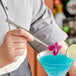 A person using Mercer Culinary Precision Plus straight fine point plating tongs to add a lemon garnish to a blue drink.