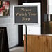 A Chef Master silver hostess/teller sign on a counter with a message that says "Please Watch Your Step"