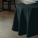 A hunter green Intedge round cloth table cover on a table with a plate on it.