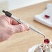 A person using Mercer Culinary curved fine point plating tongs to place a flower petal on a dessert.