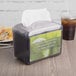 A San Jamar Venue black pearl mini interfold napkin dispenser on a table in a restaurant.