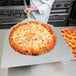 A person using an American Metalcraft aluminum pizza peel to hold a pizza.