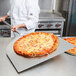 A chef using an American Metalcraft aluminum pizza peel to remove a pizza from an oven.