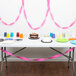 A table with a white cake and pink ribbon with a pink streamer on it.