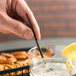 A person holding an Eco-Products black cocktail straw to a glass of liquid.