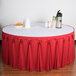 A table with a red Wyndham table skirt with Velcro clips over a white tablecloth with a bowl of oranges and a thermos.