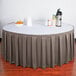 A table with a gray Snap Drape box pleat table skirt on a white tablecloth with a bowl of oranges and a thermos.