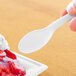 A hand holding a white Eco-Products compostable plastic spoon over a dessert.