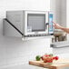 A person using a Regency stainless steel microwave shelf to heat food in a microwave.