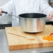 A chef holding a Vollrath Wear-Ever sauce pan over a wooden cutting board.