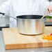 A chef using a Vollrath Wear-Ever sauce pan to cook vegetables on a cutting board.