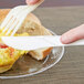 A person cutting a piece of bread with a white Eco-Products compostable plastic knife and fork.