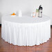 A table with a white Snap Drape box pleat table skirt on it and a bowl of oranges.