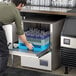 A man using a Noble Warewashing undercounter dishwasher to wash glasses.