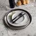 An American Metalcraft stainless steel hammered charger with a knife and fork on it.