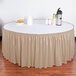 A table with a beige Snap Drape shirred pleat table skirt on a white table with a bowl of oranges and a thermos.