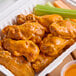 A tray of Louisiana buffalo wings with celery sticks in orange liquid.