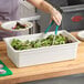 A woman using a white Cambro food pan to serve salad on a plate.