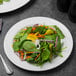 A Libbey Royal Rideau white porcelain plate with a salad of spinach, carrots, and other vegetables.