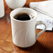 A white Libbey porcelain mug filled with brown liquid on a table.