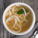 A white Libbey porcelain bouillon bowl filled with soup and noodles with a spoon.