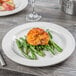 A Libbey Royal Rideau white medium rim porcelain plate with a meat dish and green beans on a table.