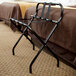 A black metal high back luggage rack with back webbing leaning against a bed.