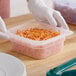 A gloved hand holding a Cambro translucent plastic container with shredded carrots.