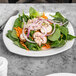 A white Libbey square porcelain plate with a salad of greens, mushrooms, onions, and carrots.