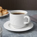 A white Libbey porcelain tea saucer with a cup of brown liquid on it.