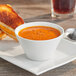 A bowl of Acopa bright white porcelain bouillon with soup and bread on a table with a grilled sandwich.