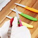 A person in gloves uses a Victorinox paring knife with a yellow handle to cut a strawberry on a wooden cutting board.