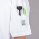 A person wearing a white Chef Revival short sleeve chef jacket with a knife and pen in the pocket.