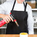 A woman in a black Chef Revival apron is spraying something on a bowl.