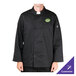 A man wearing a black Chef Revival chef jacket with a green logo on the chest in a professional kitchen.