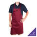 A man wearing a burgundy Chef Revival bib apron with a pocket.