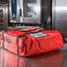 A red Rubbermaid insulated pizza delivery bag on a counter.