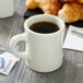 A Tuxton eggshell white china mug filled with brown liquid on a table with a cup of coffee and croissants.