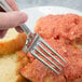 A hand holding a Bon Chef stainless steel dinner fork over a plate of food.