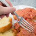 A hand holding a Bon Chef stainless steel dinner fork over a plate of food.