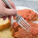 A hand holding a Bon Chef Tuscany dinner fork over a plate of food.