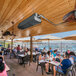 A group of people sitting at tables outdoors under a white umbrella using a Schwank natural gas patio heater.