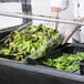 A person in gloves putting food into a Carlisle portable salad bar.